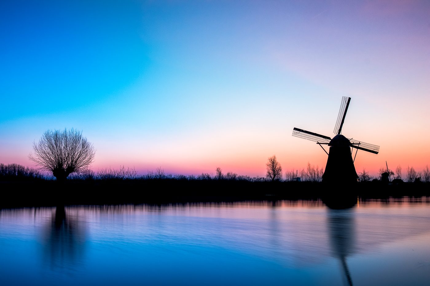 Molen in silhouet met spiegeling in het water tijdens het blauwe uur
