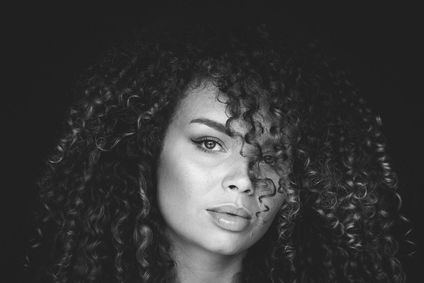Zwart-witportret van een vrouw met een grote bos krullen tegen diep zwart