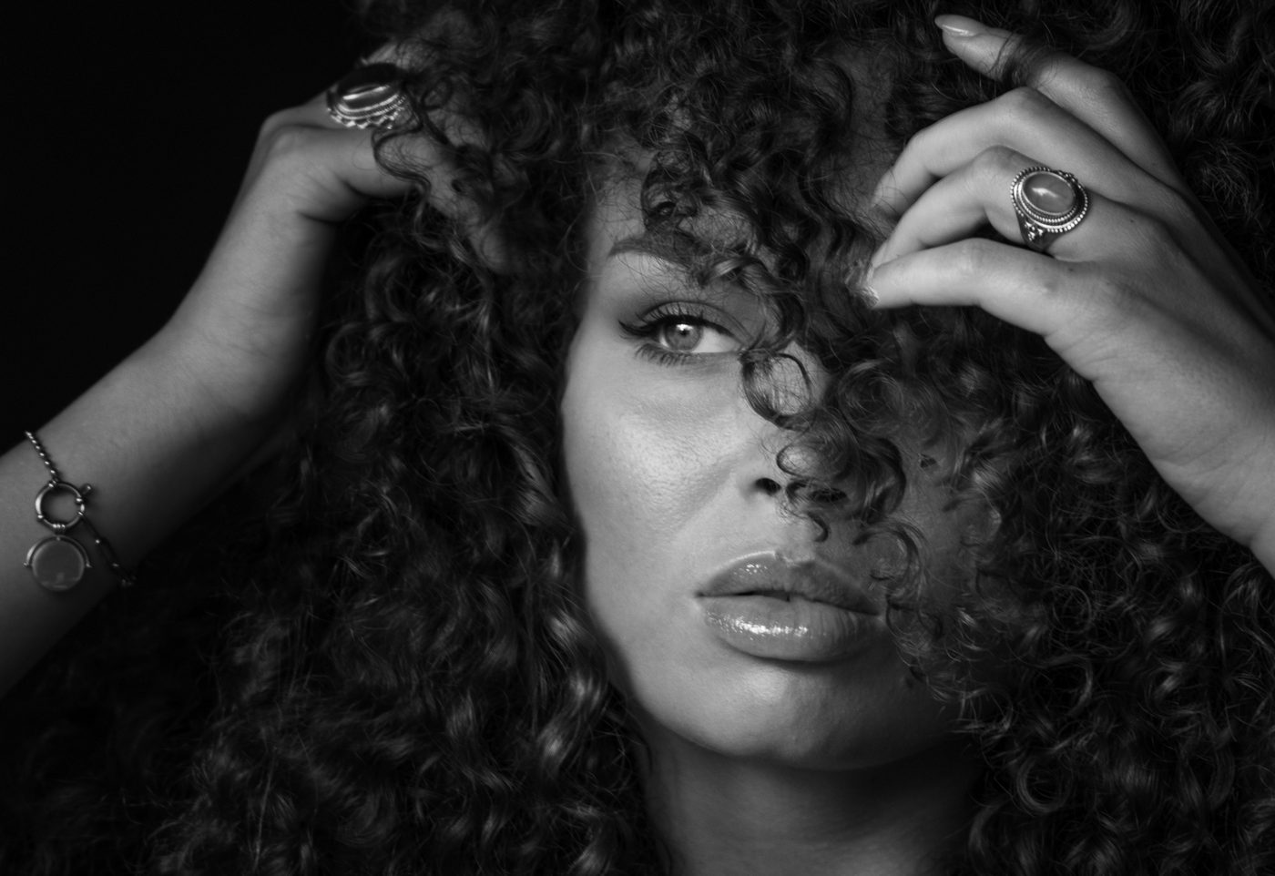 Zwart-witportret van een vrouw die haar handen in haar krullen legt