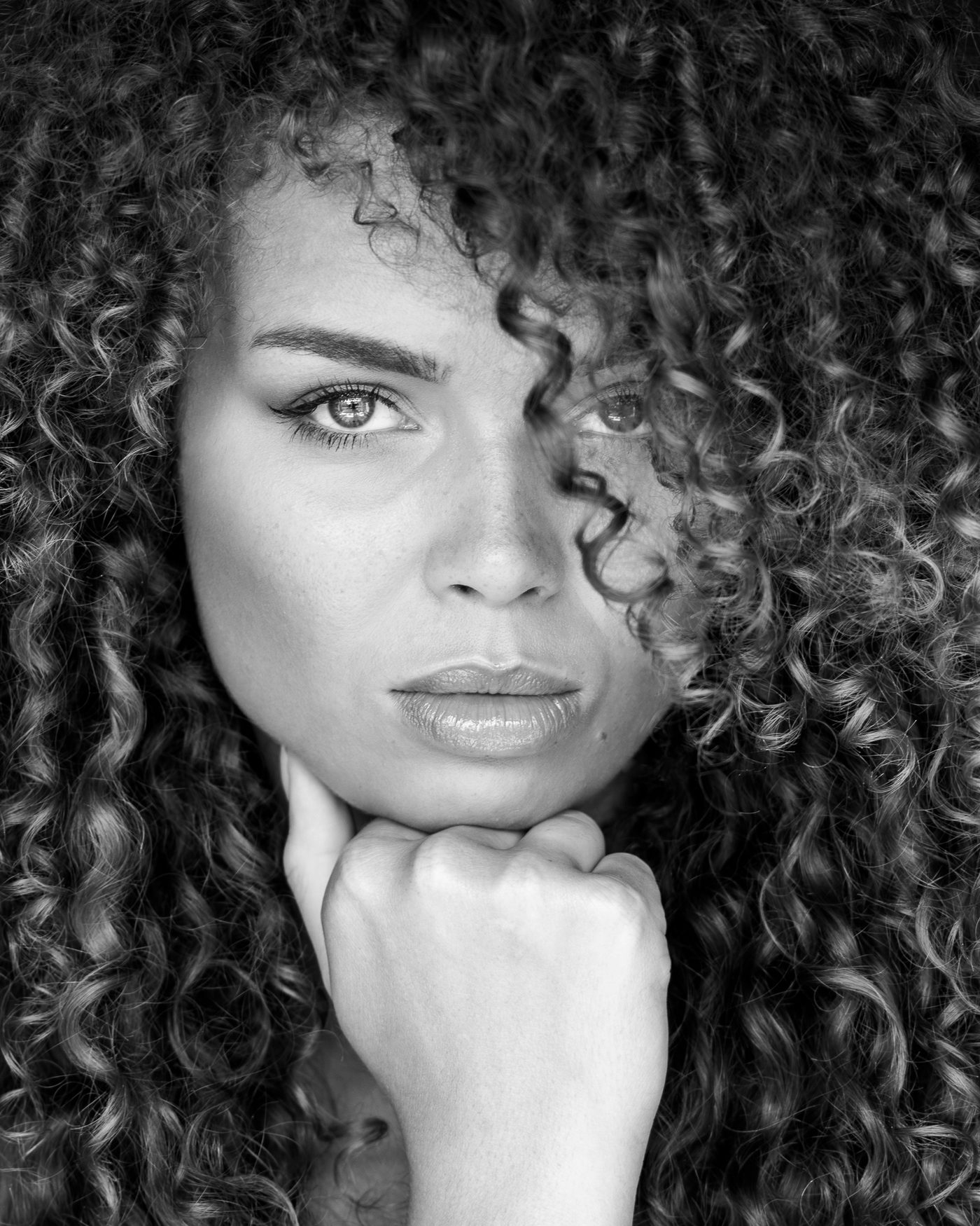 Zwart-witportret van een vrouw met lange krullen, hand onder de kin