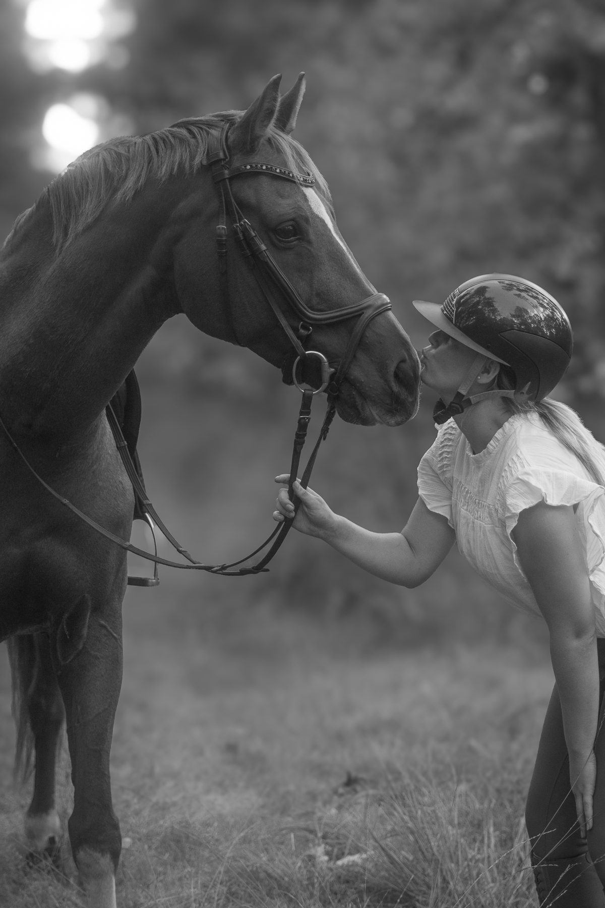 Meisje met pet neus aan neus met haar paard in tegenlicht