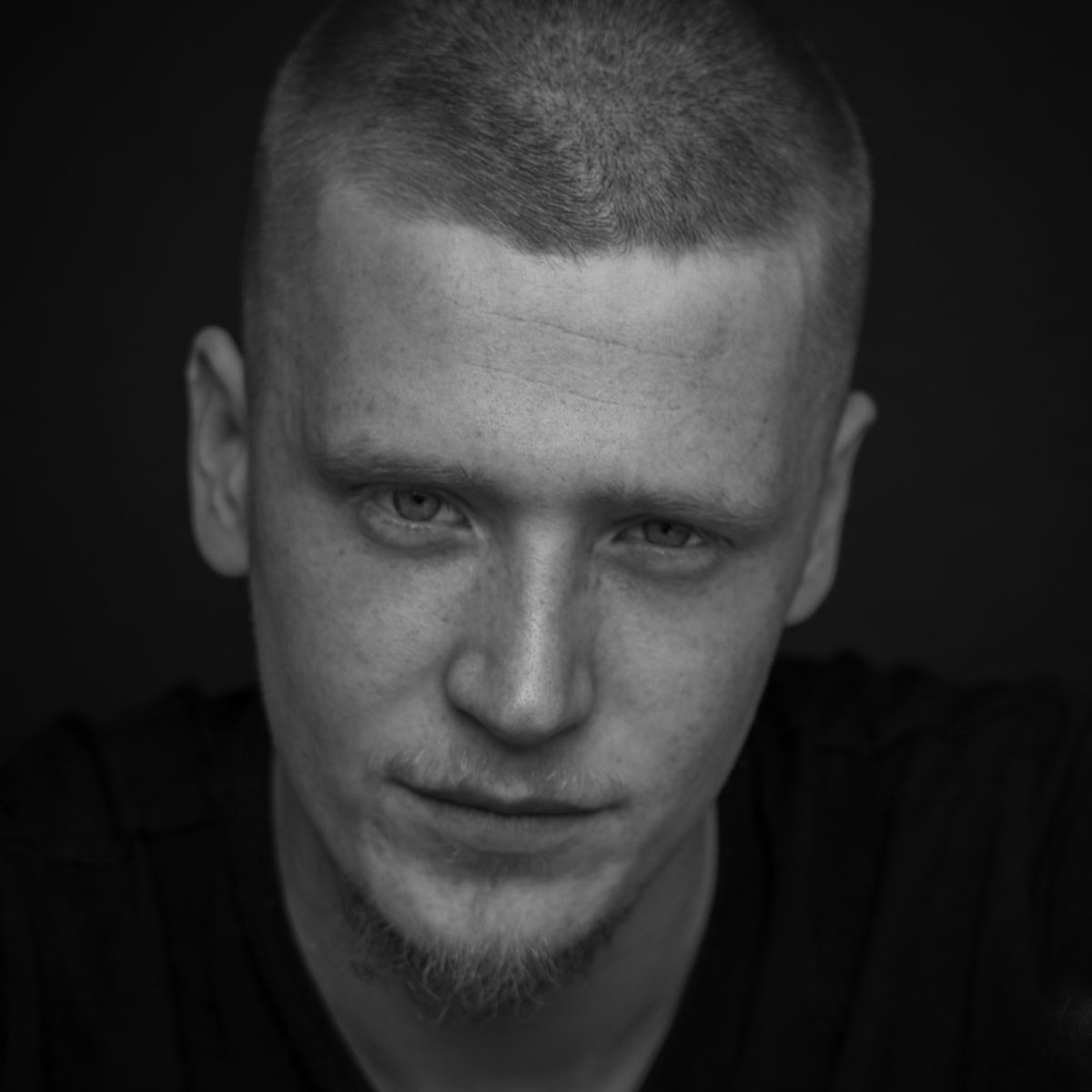 Zwart-witportret van een jonge man, ingetogen, tegen een donkere achtergrond